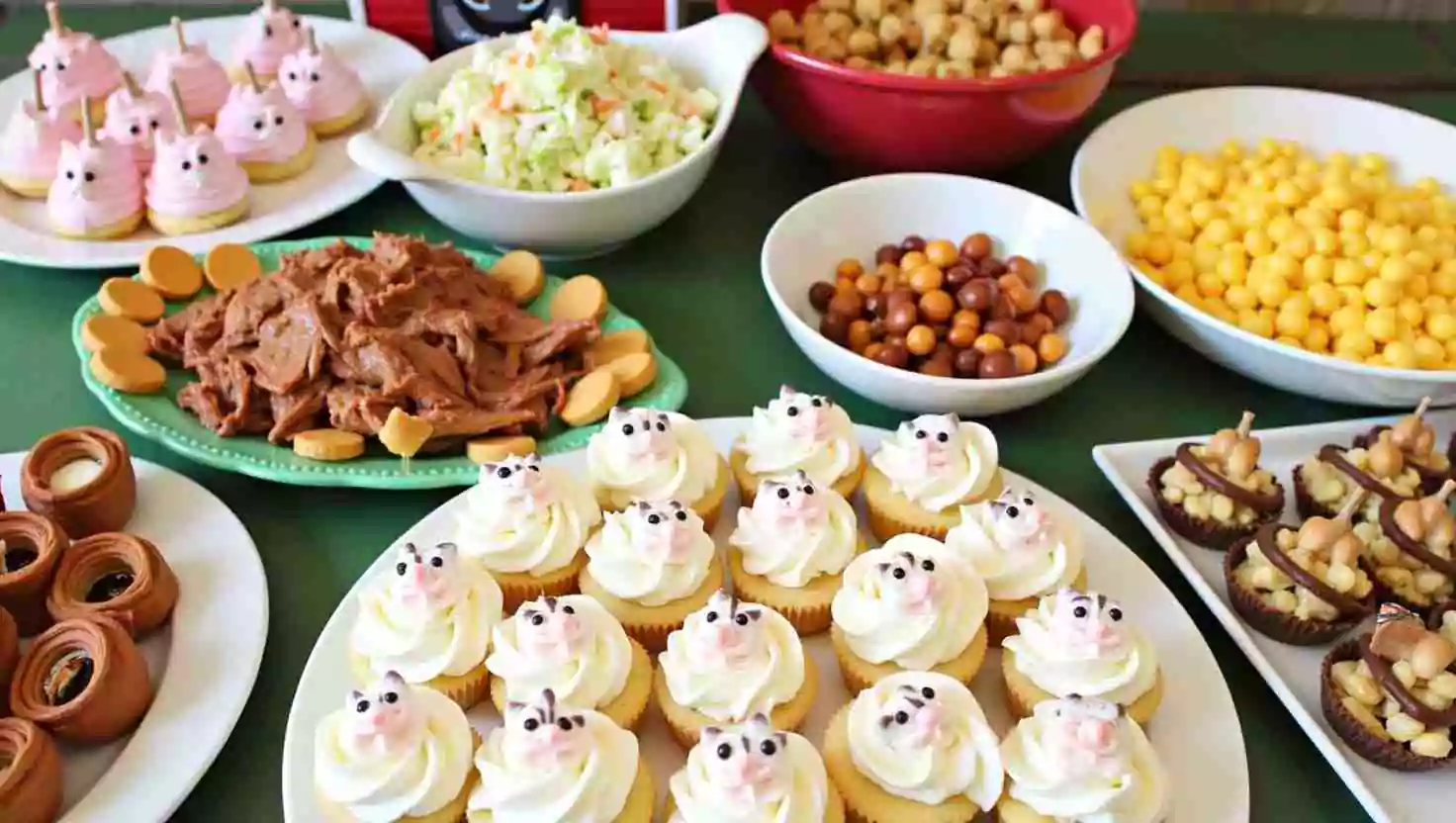 A farm-themed dessert table featuring a variety of treats, including cupcakes with pig decorations, colorful candies, coleslaw, pulled meat, and more. The food presentation adds a fun and delicious touch to the party.