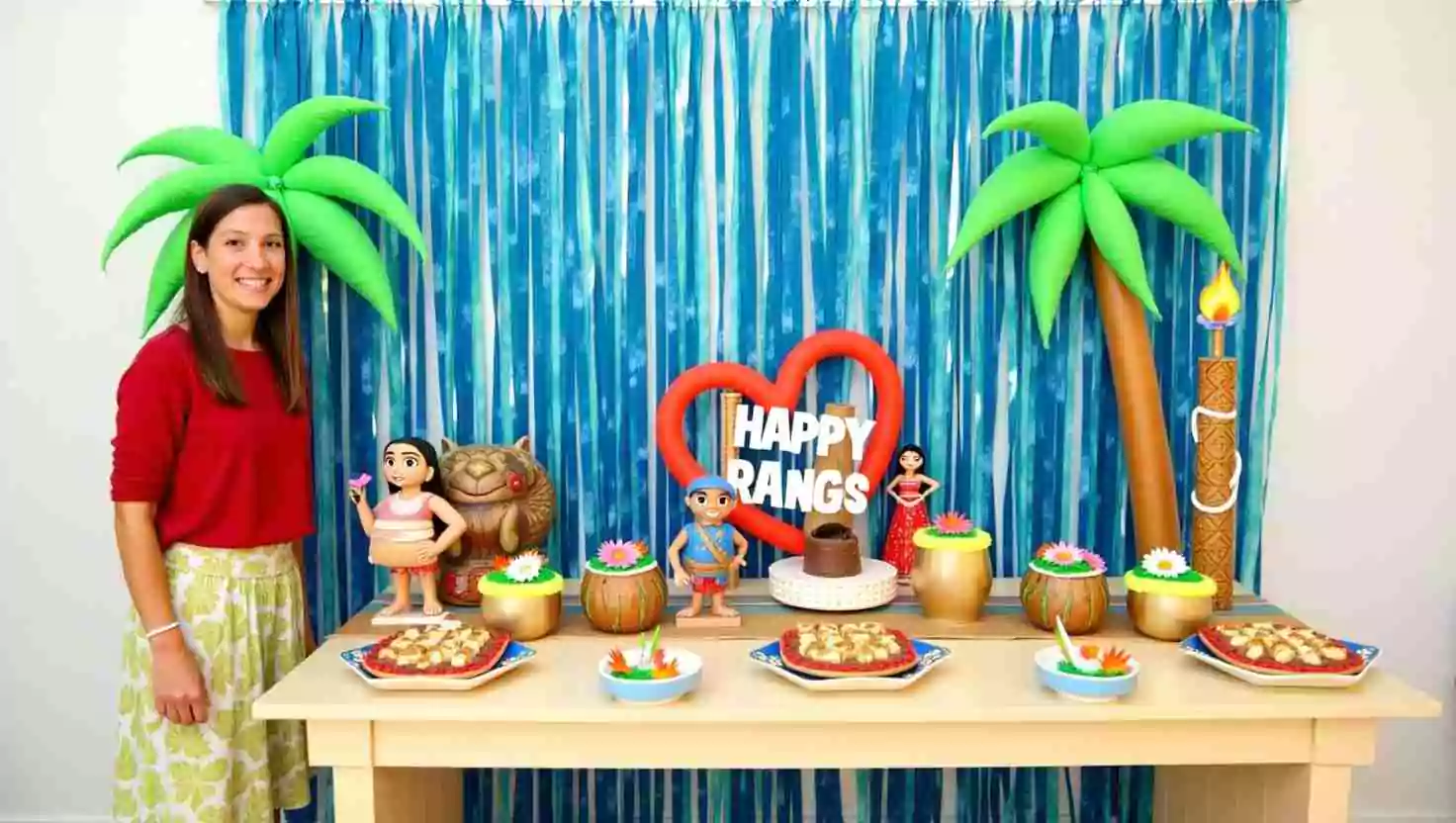 A dessert table for a Moana-themed birthday party, decorated with palm trees, tiki torches, and figurines of Moana characters. The table features tropical treats and colorful floral decorations.