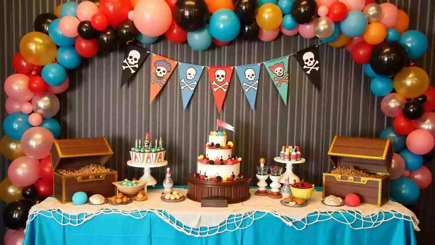 A pirate-themed dessert table featuring a tiered cake, treasure chest props, colorful balloons, and skull-and-crossbones banners. The setup is vibrant and perfect for a pirate-inspired celebration.